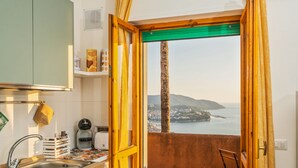 Eine kleine Küche mit Spüle, Kaffeemaschine und Meerblick durch eine offene Tür.