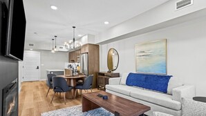 A modern living room with a sofa, coffee table, and dining area. - The Creekside - Top Floor Mountiain & Creek Views (Dead Man's Flats)