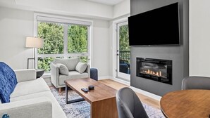 A modern living room with a fireplace, a flat-screen TV, and a sofa. - The Creekside - Top Floor Mountiain & Creek Views (Dead Man's Flats)