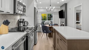 A modern kitchen with white cabinetry, stainless steel appliances, a central island, and pendant lighting.