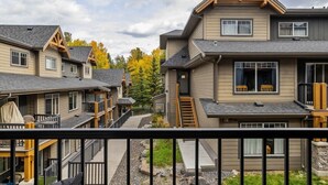 A row of modern multi-story homes with balconies, a central walkway, and a view of autumn trees.