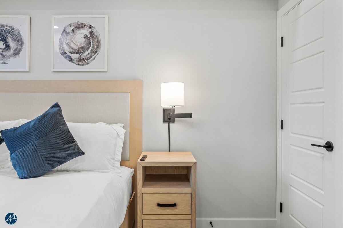 Una habitación de hotel con una cama, una mesita de noche y una lámpara, y una puerta.