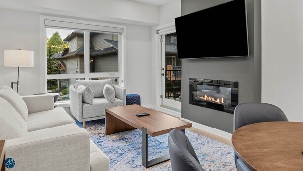 A modern living room with a fireplace, a flat-screen TV mounted on the wall, and a large window offering a view of neighboring houses.