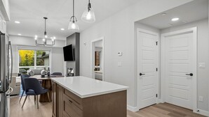 A modern kitchen with a central island, pendant lighting, and a dining area with a view of the outdoors.