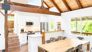 A modern kitchen with white cabinets, a central island, and a dining area with a wooden table and metal chairs. - Sage House - Walking Distance to Lake, Hot Tub, Pet Friendly w/ New AC (Arnold)
