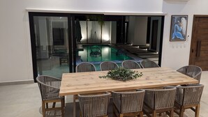 Uma área de refeições com vista para a piscina, cadeiras de vime e uma mesa de madeira.