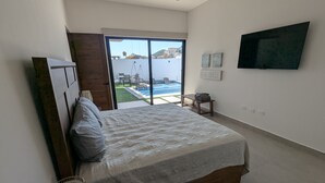 Quarto com cama grande, TV na parede e vista para piscina e edifícios.