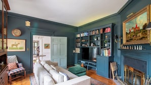 Een woonkamer met een bank, een boekenkast, een open haard en een schilderij aan de muur.
