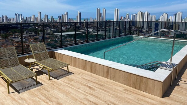 A rooftop pool with a city view, lounge chairs, and a wooden deck. - Bela Hospedagem - Compact Time 907 (João Pessoa)