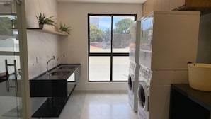 A modern kitchen with a built-in washing machine, a large window, and a plant on the wall. - Bela Hospedagem - Compact Time 907 (João Pessoa)