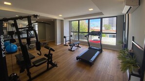 A gym with exercise equipment, a treadmill, and large windows offering a view of the outside. - Bela Hospedagem - Compact Time 907 (João Pessoa)