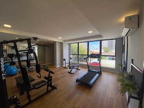 A gym with exercise equipment, a treadmill, and large windows. - Bela Hospedagem - Compact Time 907 (João Pessoa)