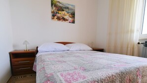 Une chambre à coucher avec un lit, deux tables de chevet, une commode, un tableau au mur et une fenêtre avec des rideaux.