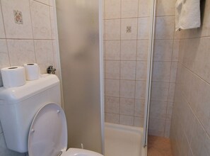 Ein Badezimmer mit Toilette, zwei Toilettenpapierrollen, einer Dusche und einem Handtuchhalter.