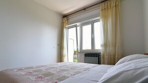 A bedroom with a bed, a window with curtains, and a radiator.