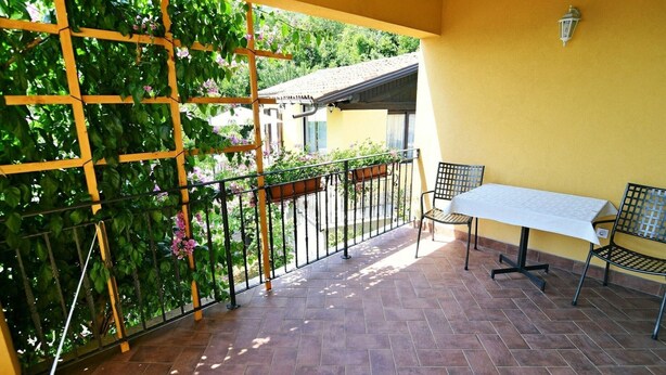 A balcony with a table and chairs, a wooden trellis with climbing plants, and a yellow wall.