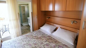 A bedroom with a bed, wooden wardrobe, and a bathroom visible through an open door.