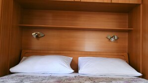 A bed with white pillows and a floral-patterned bedspread in a wooden room with a slatted headboard and two wall-mounted light fixtures.