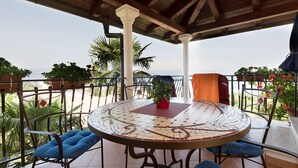 A covered outdoor patio with a round mosaic table, blue cushioned chairs, and potted plants.
