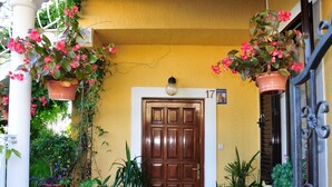 A wooden door with a number 17 sign, surrounded by potted plants and a small table with a chair.