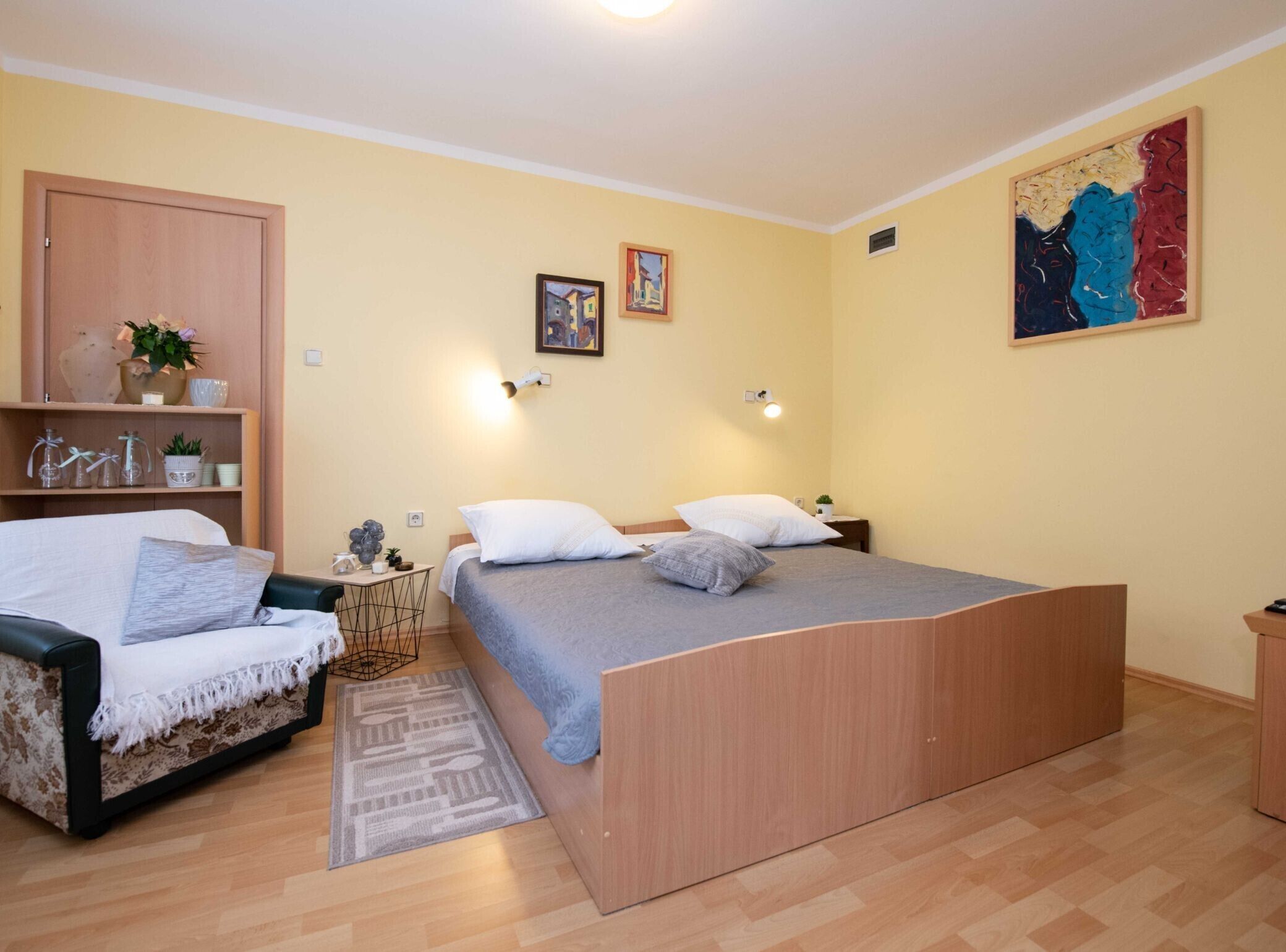 Une chambre à coucher comprenant un lit, un canapé, une petite table, une étagère avec des objets décoratifs et un tableau au mur.