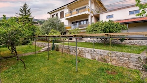 Ein zweistöckiges Haus mit Balkon, umgeben von einer Steinmauer und einem Rasengarten.