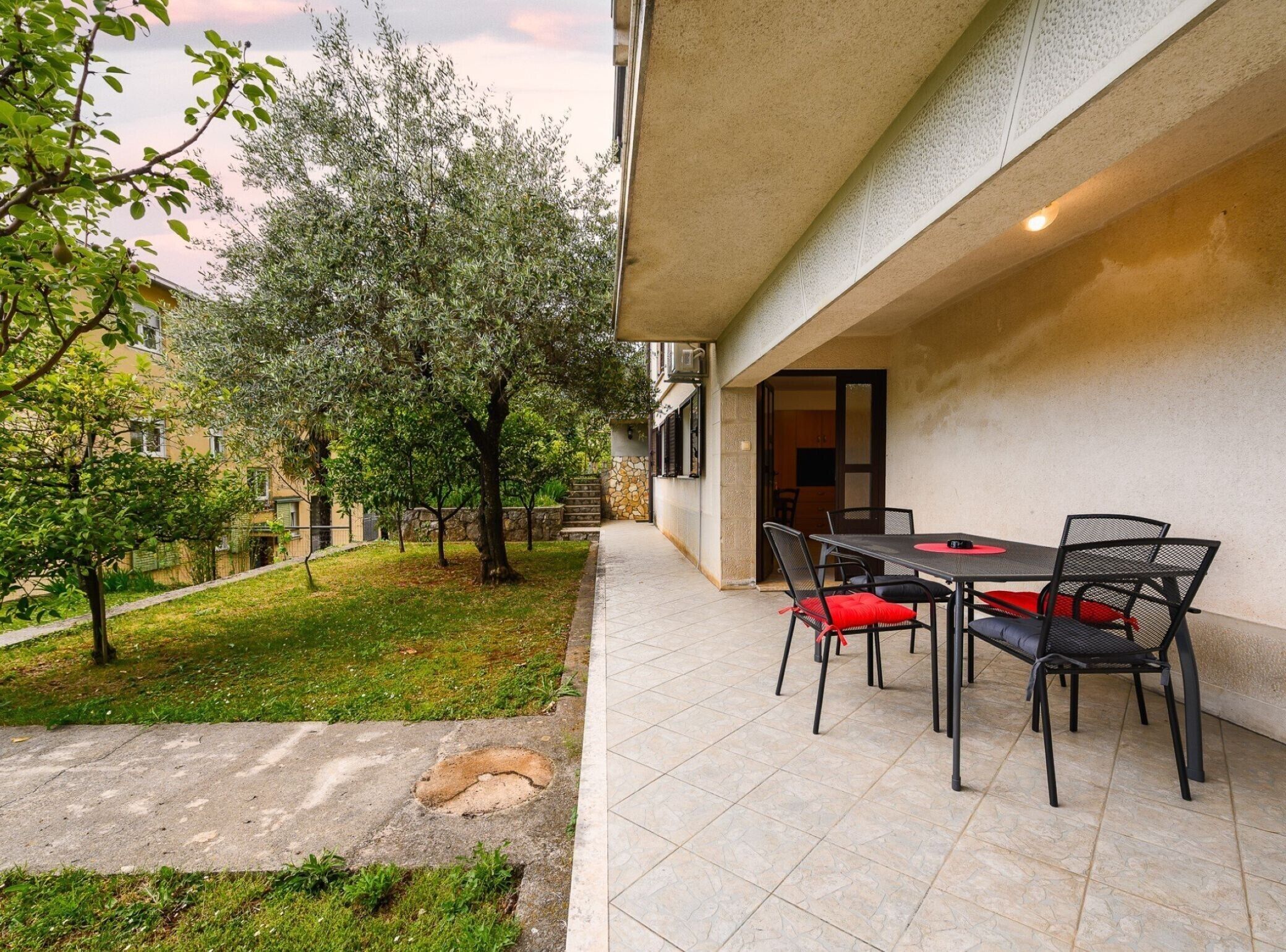 An outdoor patio with a table and chairs, a grassy area with trees, and a building entrance.