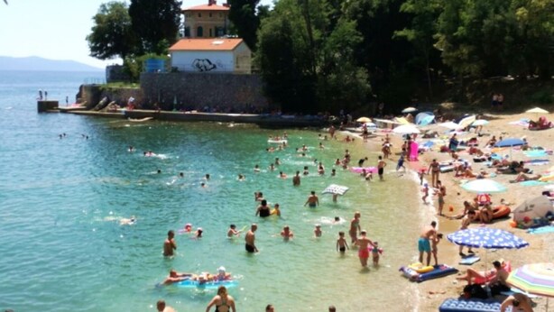 A crowded beach with people swimming and sunbathing, a stone wall, and a building with a red roof. - Cozy Lovran Apartment with Balcony - Two Bedroom Apartment with Sea View and Balcony (Lovran)