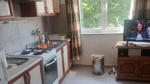 A compact kitchen with a stove, sink, and a small trash bin. A television is mounted on a wooden cabinet to the right. - Cozy Lovran Apartment with Balcony - Two Bedroom Apartment with Sea View and Balcony (Lovran)