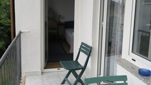 A balcony with a green chair, a blue bowl, and a view of a room with a bed and a chair. - Cozy Lovran Apartment with Balcony - Two Bedroom Apartment with Sea View and Balcony (Lovran)