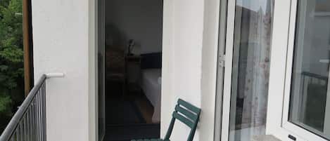 A balcony with a green chair, a blue bowl, and a view of a room with a bed and a chair.