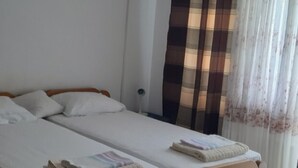 A double bed with white linens and two pillows, a wooden headboard, and a window with a striped curtain. - Cozy Lovran Apartment with Balcony - Two Bedroom Apartment with Sea View and Balcony (Lovran)