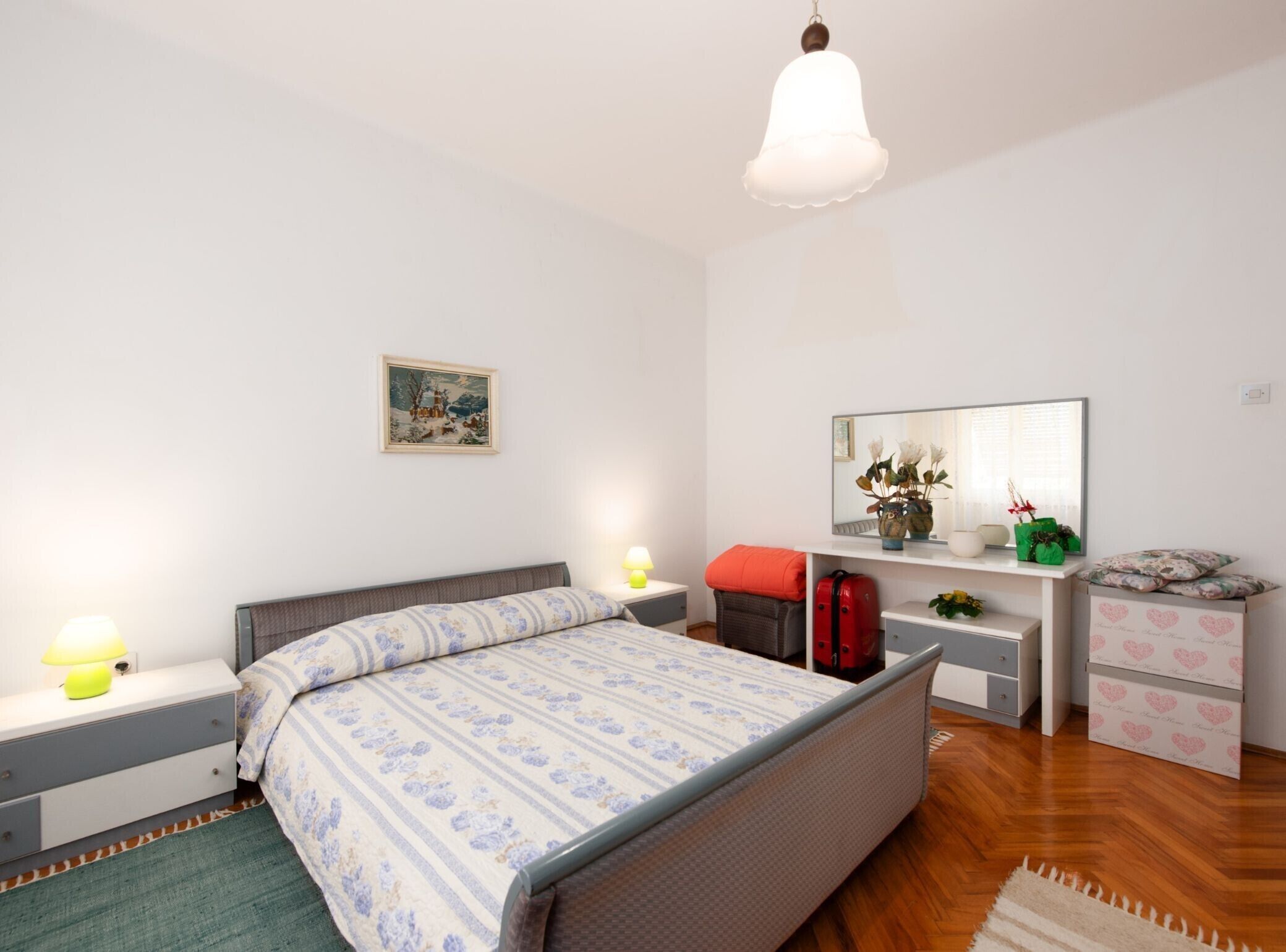 A bedroom with a bed, bedside tables, a dresser, a mirror, and a hanging light fixture.