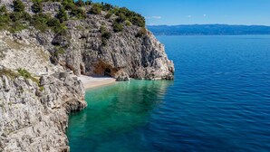 Une côte rocheuse bordée d’eaux turquoise et cristallines, avec une petite plage.