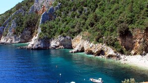 Un paysage côtier avec des falaises rocheuses, une eau turquoise et limpide, et plusieurs petits bateaux ancrés près du rivage.