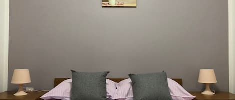 A bedroom with a bed, two pillows, a nightstand with a lamp, and a wall-mounted picture.