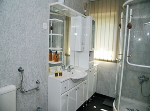 Un baño moderno con ducha envuelta en vidrio, un lavamanos blanco con espejo arriba y pared con azulejos de mármol.