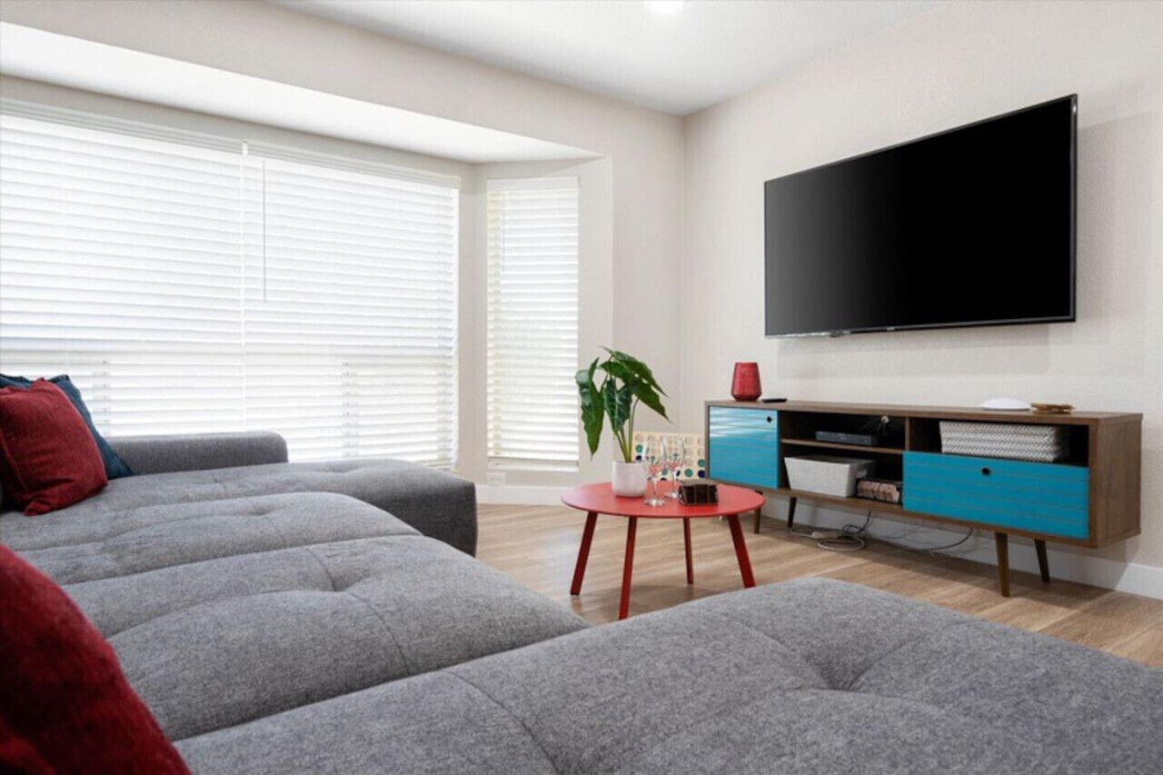 Un soggiorno moderno con un divano grigio, un tavolino da caffè rosso e una TV a schermo piatto montata a parete.