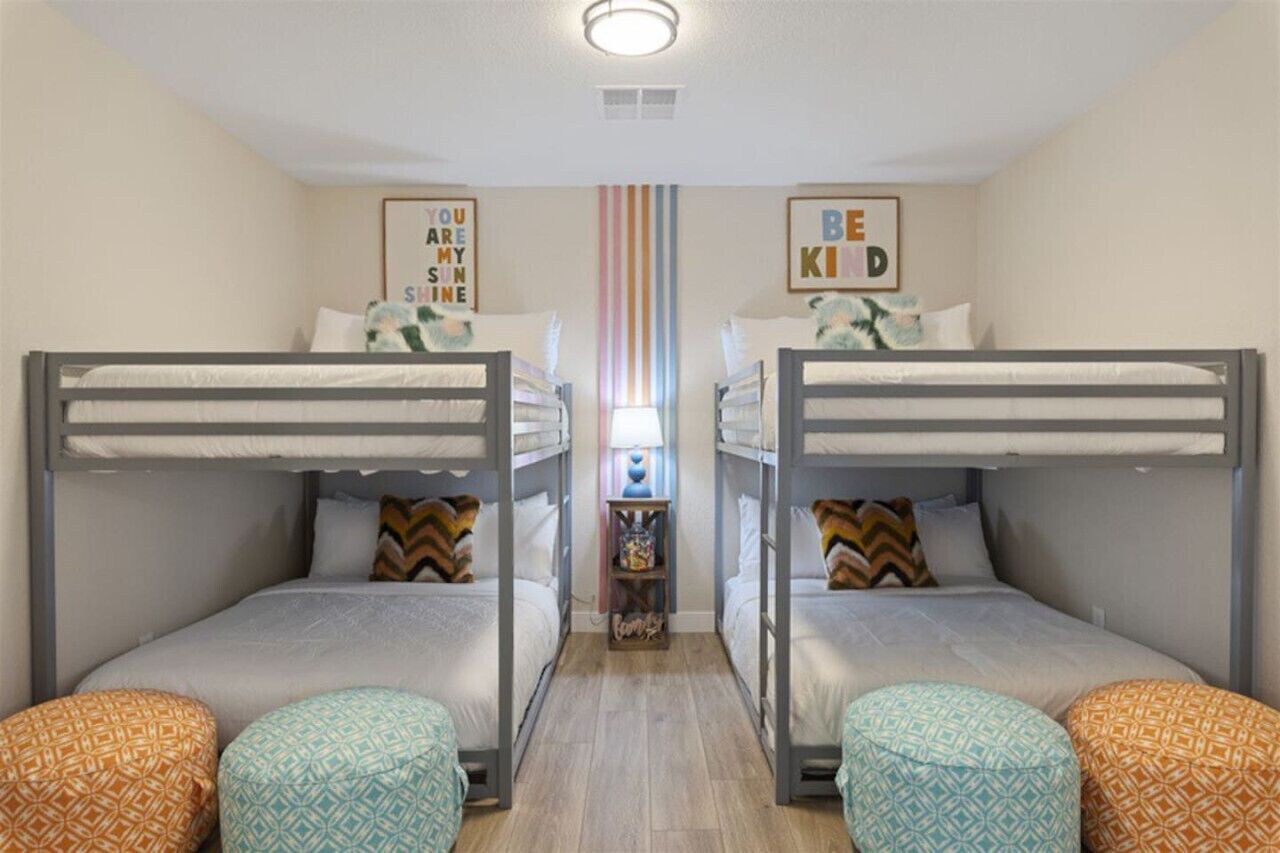A room with two bunk beds, a small table with a lamp, and colorful pillows.