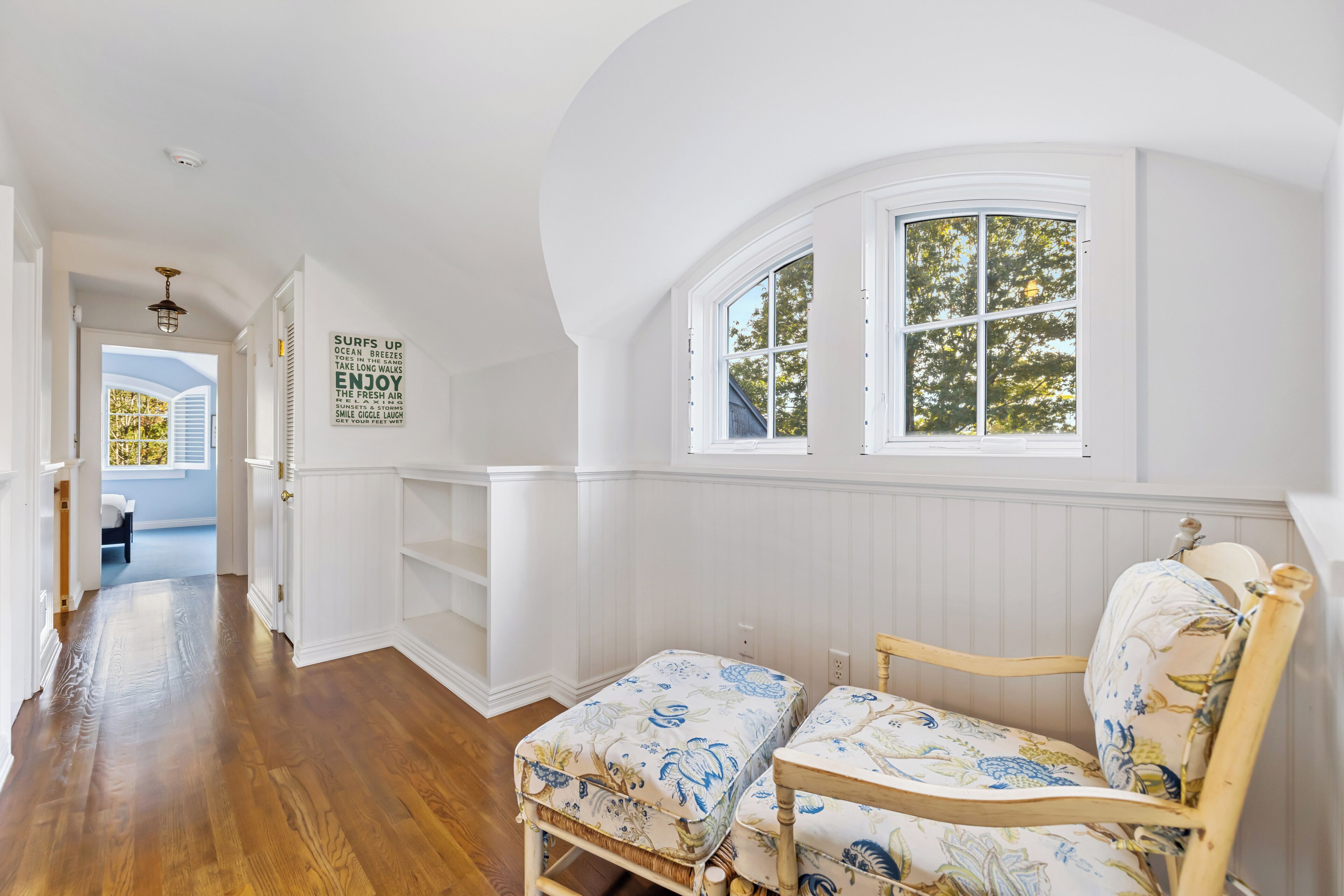A room with a wooden floor, a bench with floral upholstery, and a window with a view of trees.