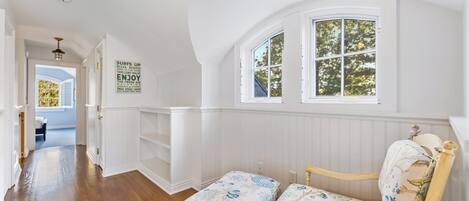 A room with a wooden floor, a bench with floral upholstery, and a window with a view of trees.
