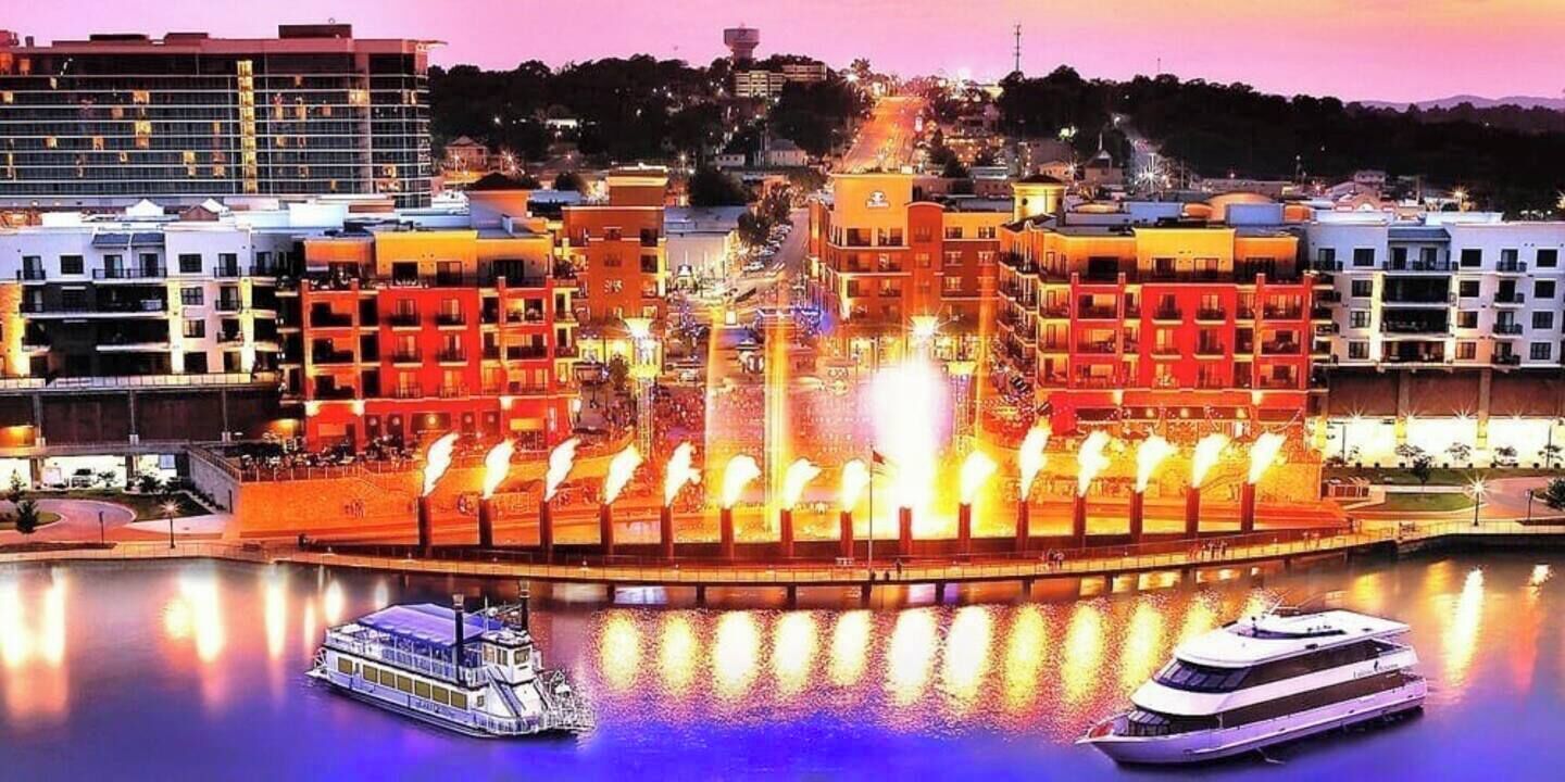 A waterfront hotel with a central fountain, multiple balconies, and boats docked in the water.