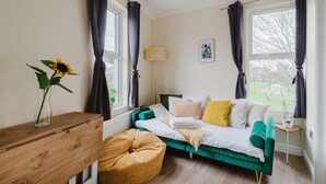 Ein Zimmer mit einem grünen Sofa, einem Holztisch, einer Vase mit einem Sonnenblume und einem Fenster mit Vorhängen.