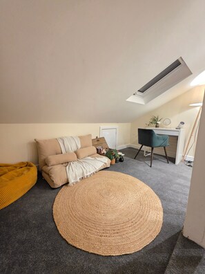 Un dormitorio estilo loft acogedor con un ventanal grande, un sofá cómodo, un tapete redondo tejido y un escritorio con silla.