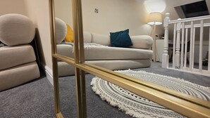 Ein Wohnzimmer mit einem beigefarbenen Sofa, einem weißen Sessel, einem runden Teppich und einem weißen Babybett.