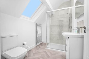 A modern bathroom with a skylight, a glass shower enclosure, and a white sink.