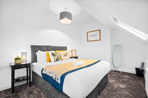 A modern bedroom with a large bed, a bedside table with a lamp, a framed picture on the wall, and a ceiling fan. - Luxury Apartment - Netflix - On Street Parking (Birmingham)
