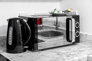 A Breville toaster with a transparent glass door, a kettle, and a plate with food items on the countertop.