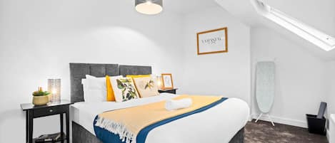 A modern bedroom with a large bed, a bedside table with a lamp, a framed picture on the wall, and a ceiling fan.