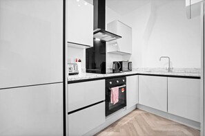 A modern kitchen with white cabinetry, a black oven, a stainless steel range hood, and a marble countertop. - Luxury Apartment - Netflix - On Street Parking (Birmingham)